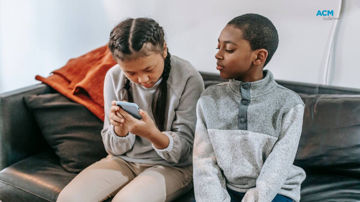 Two children sit on a couch playing with a mobile. File picture.